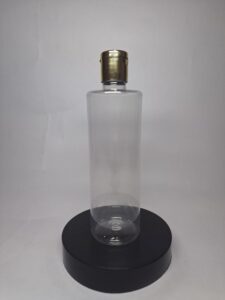 Clear cylindrical bottle with gold cap for premium bottle packaging, displayed on a black round platform.