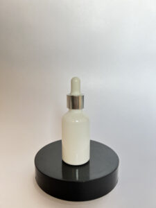  White frosted glass cosmetic packaging dropper bottle with silver collar, displayed on a black round platform. 